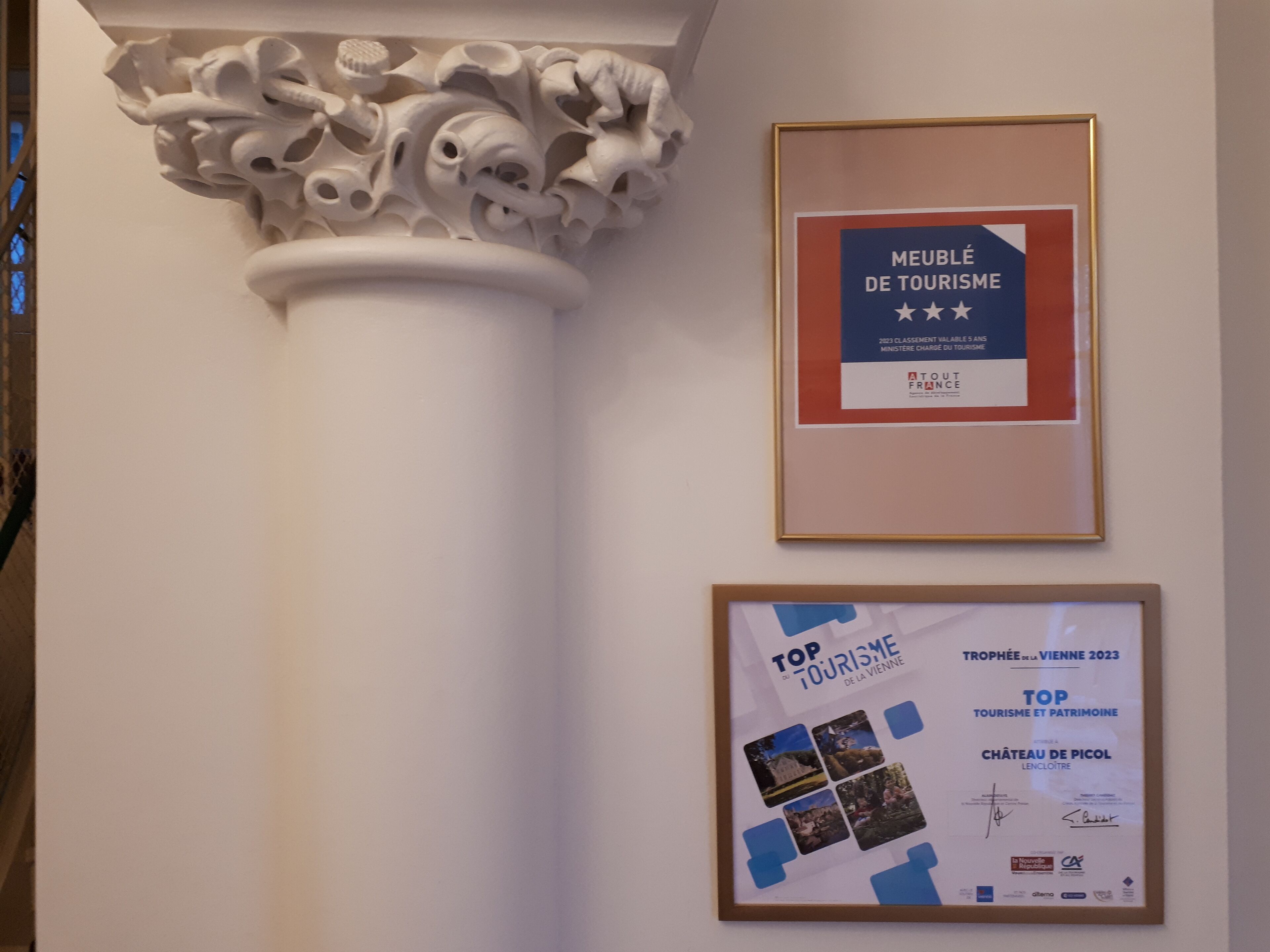 A framed award certificate for 'Meuble de Tourisme' and another for 'Top Tourisme et Patrimoine' on a wall.