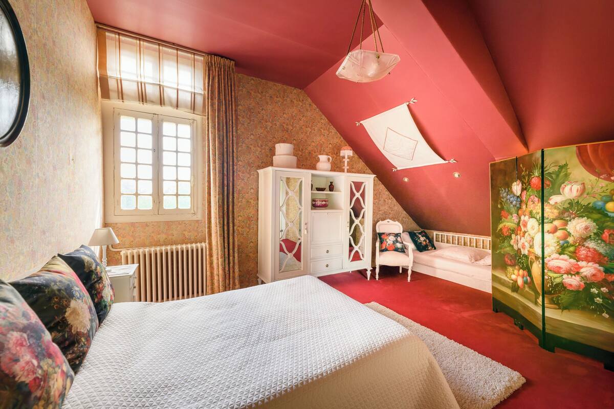 A bedroom with a large bed, a white dresser, a white chair, and a painting of flowers.
