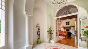 A spacious hallway with a red carpet, a large chandelier, and a view into a living area with a fireplace. - Château Picol (Lencloitre)