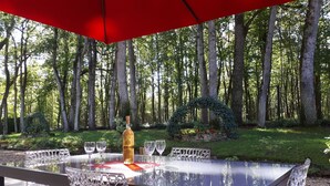An outdoor dining area with a glass table and chairs, a bottle of wine, and a red umbrella. - Château Picol (Lencloitre)