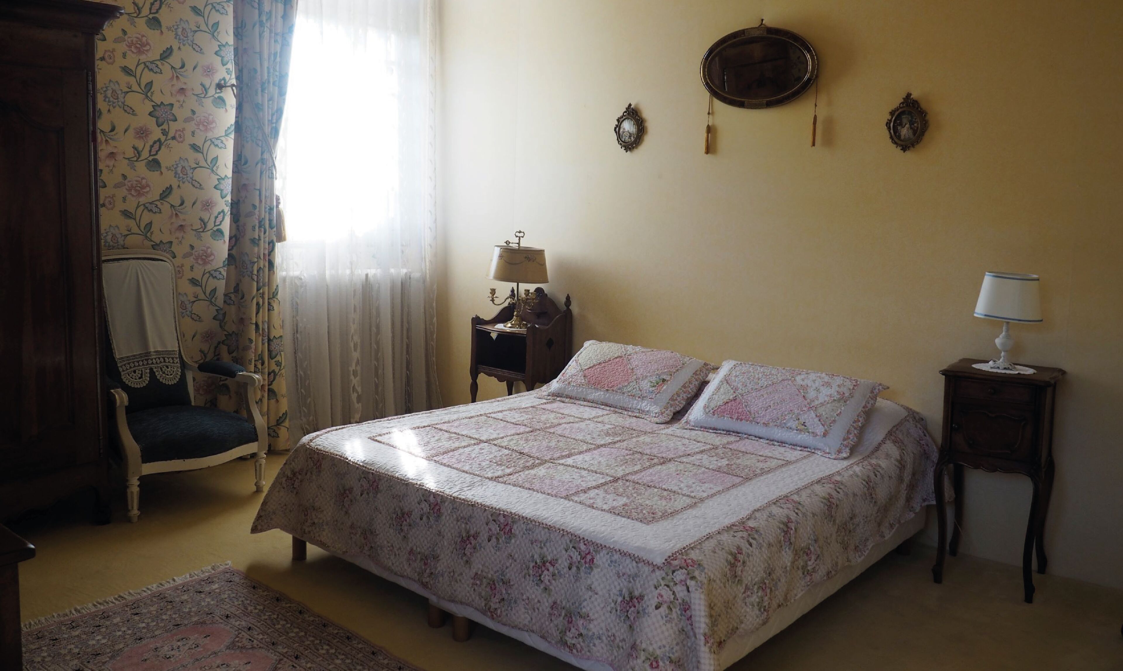 Un dormitorio con una cama, dos mesitas de noche, una silla y una ventana con cortinas.