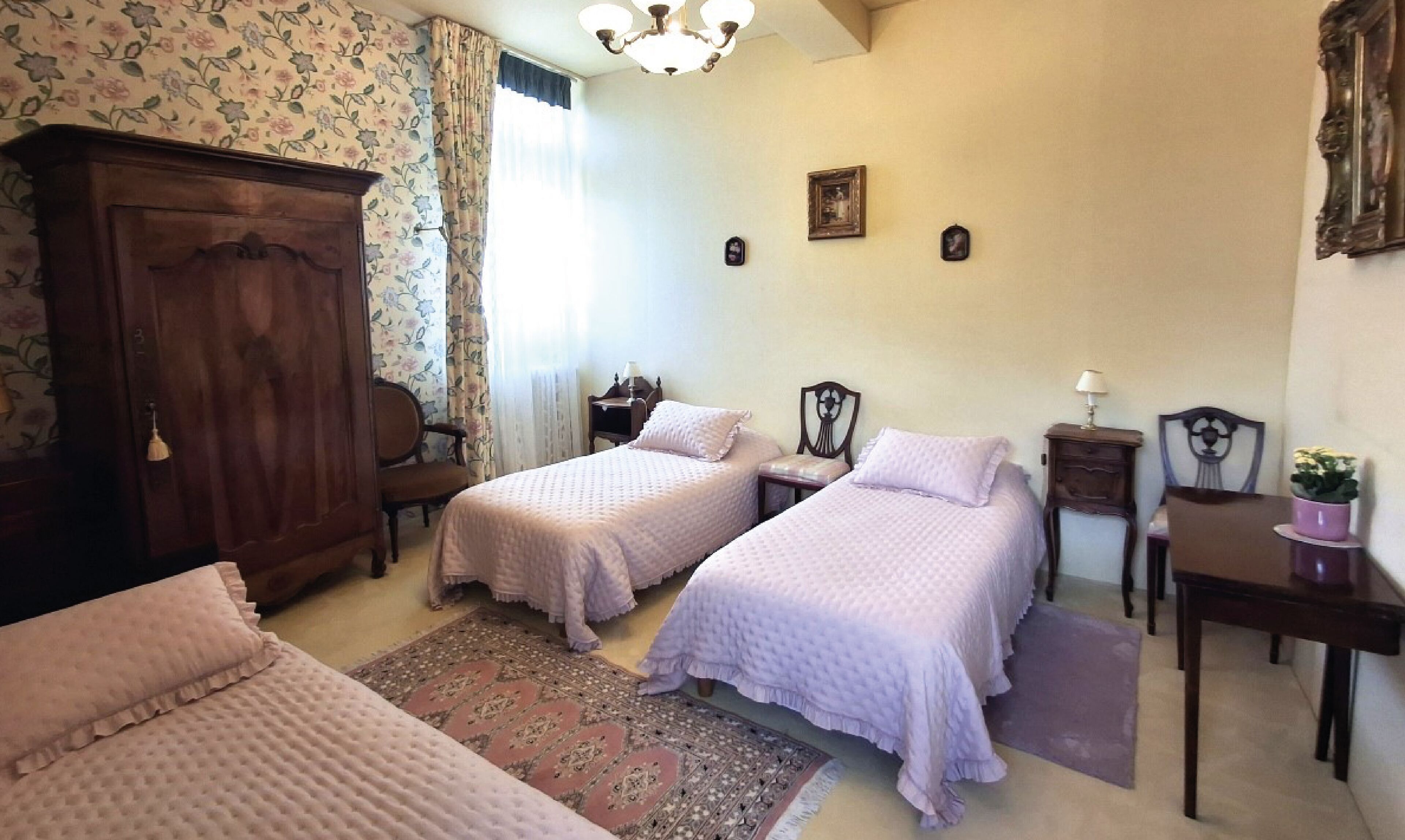 A bedroom with two beds, a wooden wardrobe, a desk, and a chair.