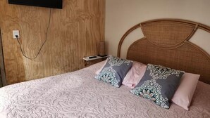 Un dormitorio con pared de madera, un televisor de pantalla plana montado sobre la cama y un cabecero de mimbre.