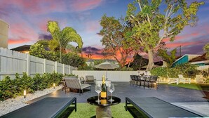 Une terrasse extérieure avec une table dressée pour deux personnes, entourée de fauteuils et offrant une vue sur le coucher du soleil.