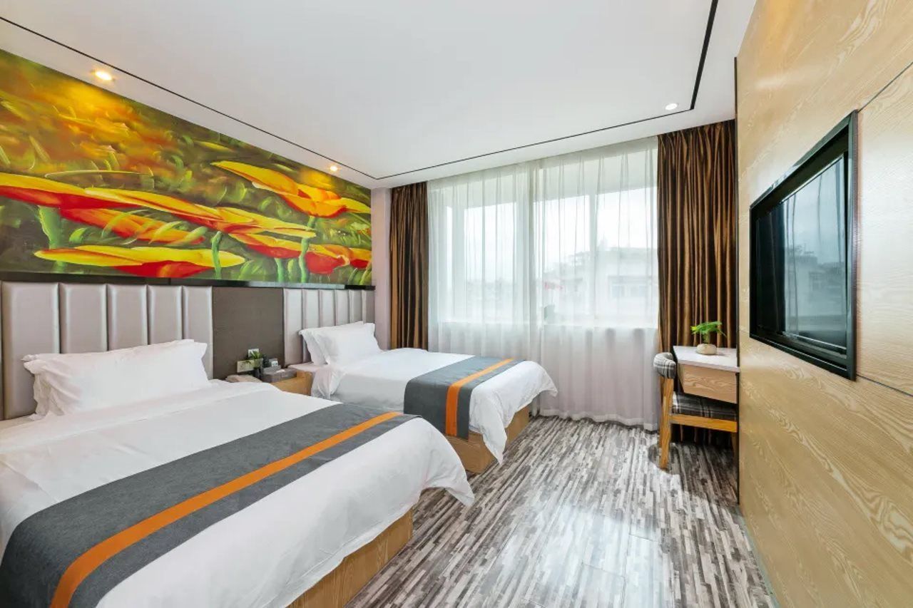 A hotel room with two beds, a desk, a TV, and a large window with curtains.