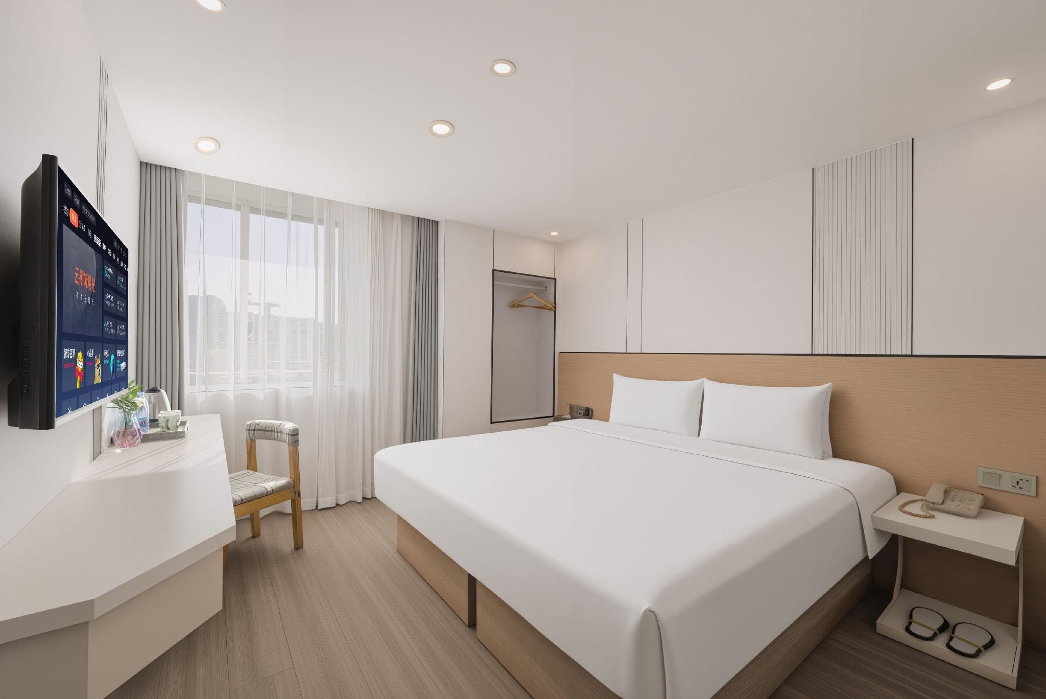 Habitació d'hotel amb un llit gran, una taula de nit amb un telèfon, una cadira, un escriptori amb un televisor i una finestra amb cortines.