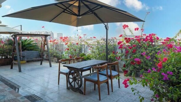 Eine Terrasse im Freien mit Tisch und Stühlen, einem großen Sonnenschirm und blühenden Blumen.