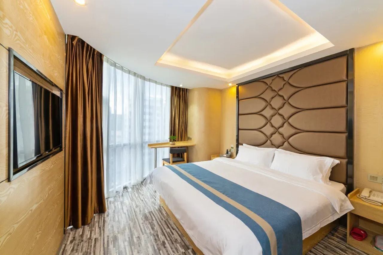 Een hotelkamer met een groot bed, een nachtkastje, een raam met gordijnen en een aan de muur bevestigde televisie.