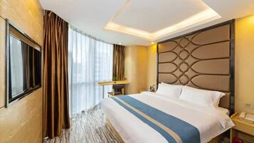 Een hotelkamer met een groot bed, een nachtkastje, een raam met gordijnen en een aan de muur bevestigde televisie.