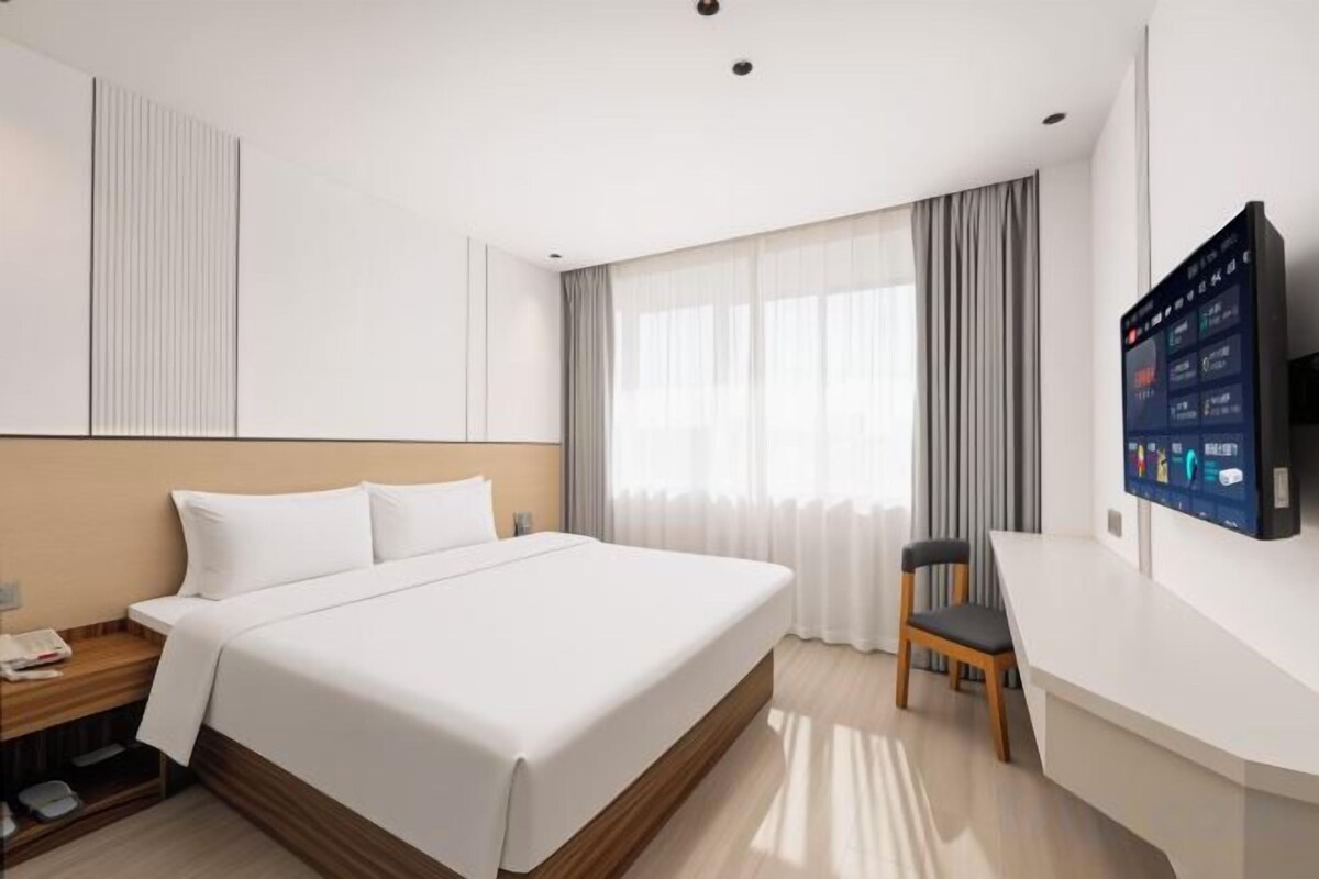A hotel room with a large bed, a desk, a chair, and a TV mounted on the wall.