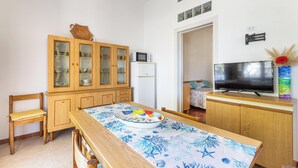 Un espace de vie compact comprenant une table à manger en bois, des chaises, un meuble avec des portes en verre, un four à micro-ondes, un réfrigérateur, un téléviseur et une porte donnant sur une autre pièce.