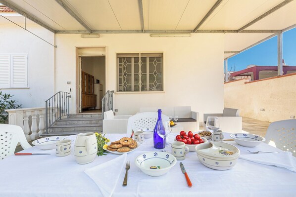 A dining table set with plates, bowls, glasses, and cutlery, with a view of a building and a staircase in the background.