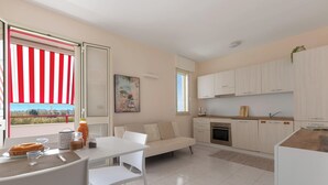 Una cucina moderna con mobili bianchi, un'area pranzo con tavolo e sedie bianche e un'ampia finestra con persiana a righe rosse e bianche.