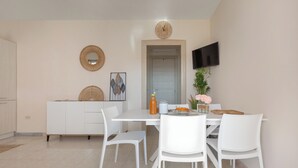 Un'area pranzo moderna con un tavolo e sedie bianche, una TV a schermo piatto montata a parete e decorazioni artistiche alle pareti.