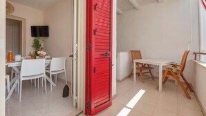 Un'area pranzo con tavolo e sedie bianche, una porta rossa e un televisore montato a parete.
