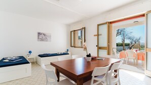 Una habitación luminosa con una mesa de comedor de madera, sillas blancas y un amplio ventanal.