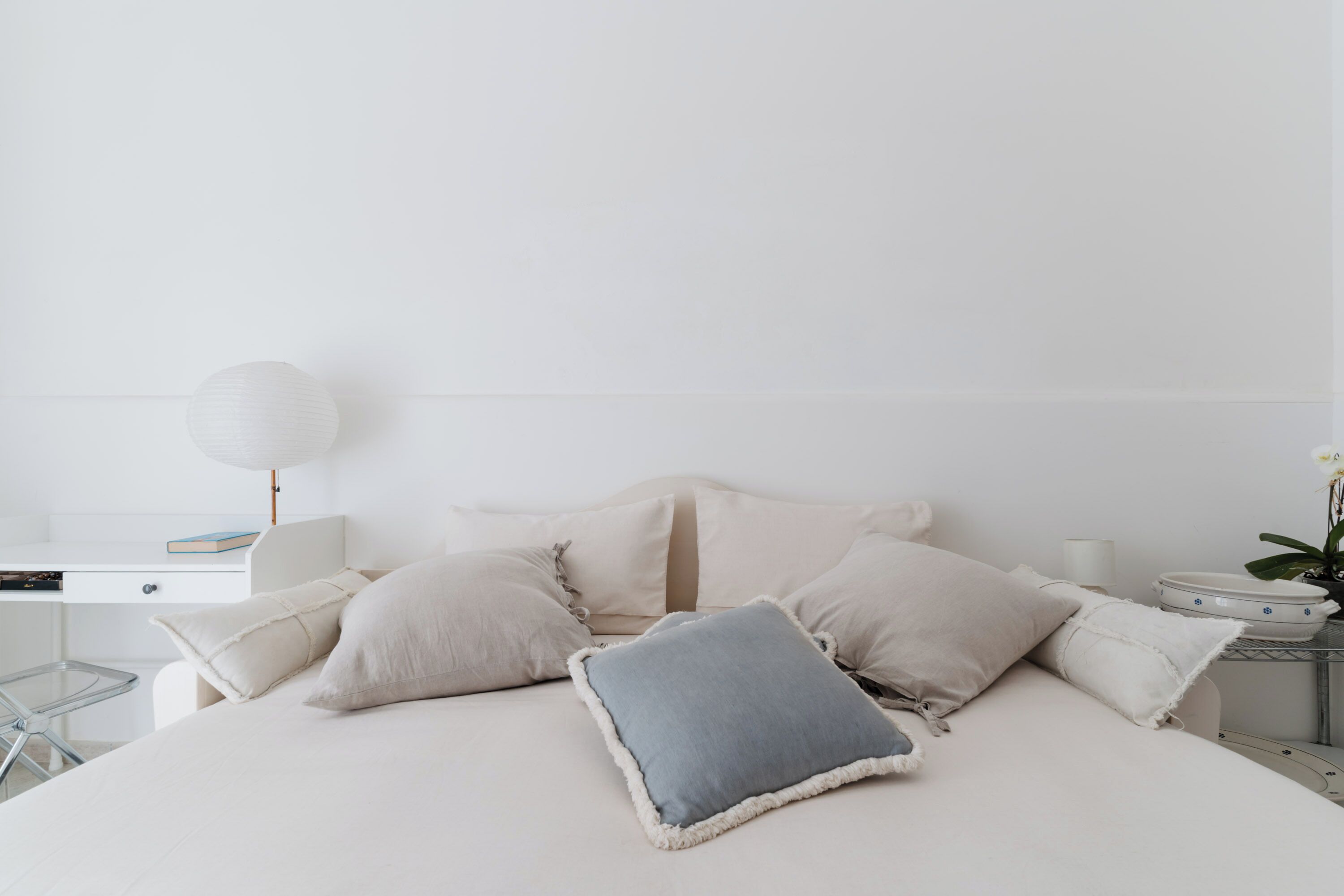 Een minimalistische slaapkamer met een bed, nachtkastjes, een lamp en een kleine plant.