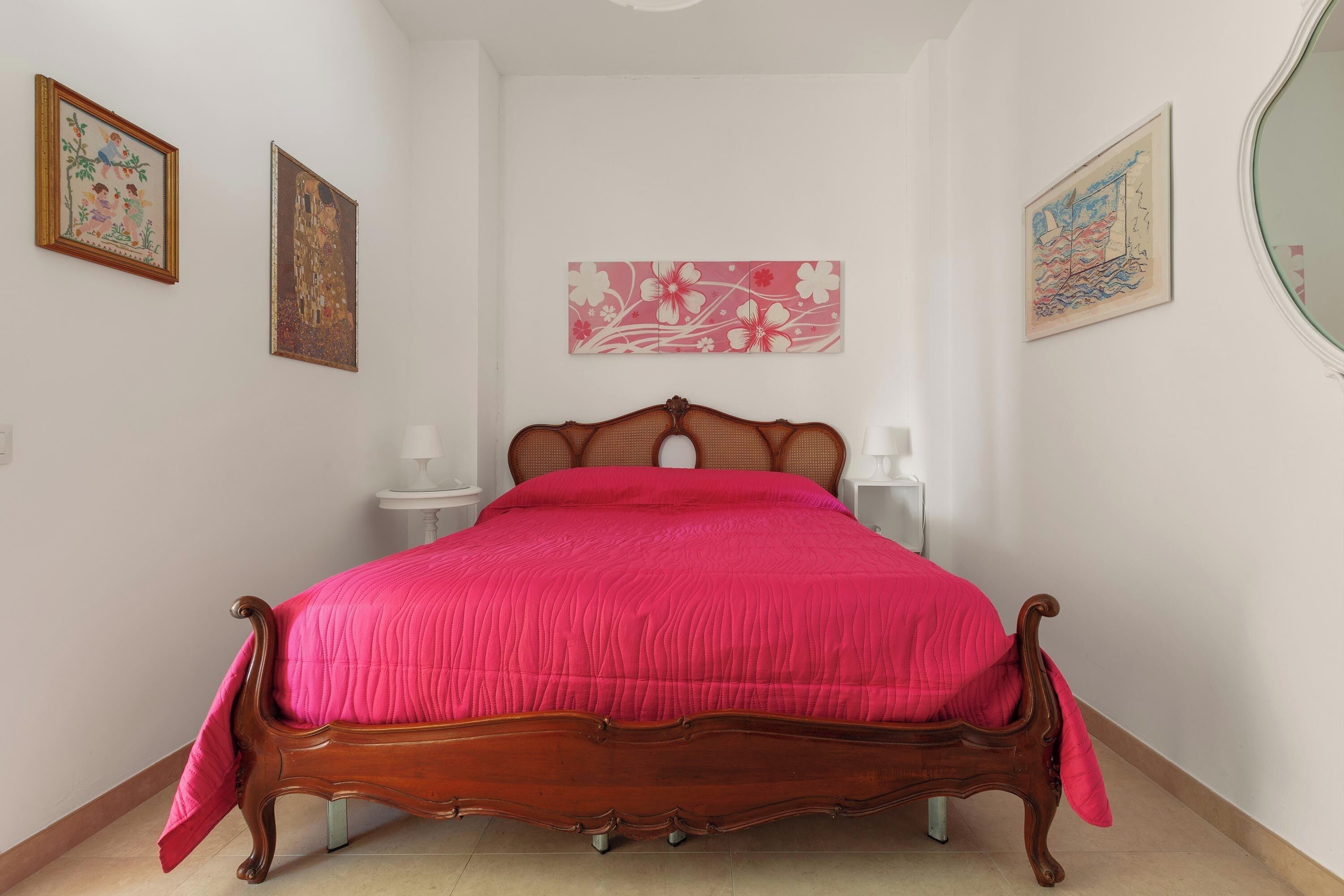 Un dormitorio con una cama de madera, paredes blancas y tres obras de arte enmarcadas.