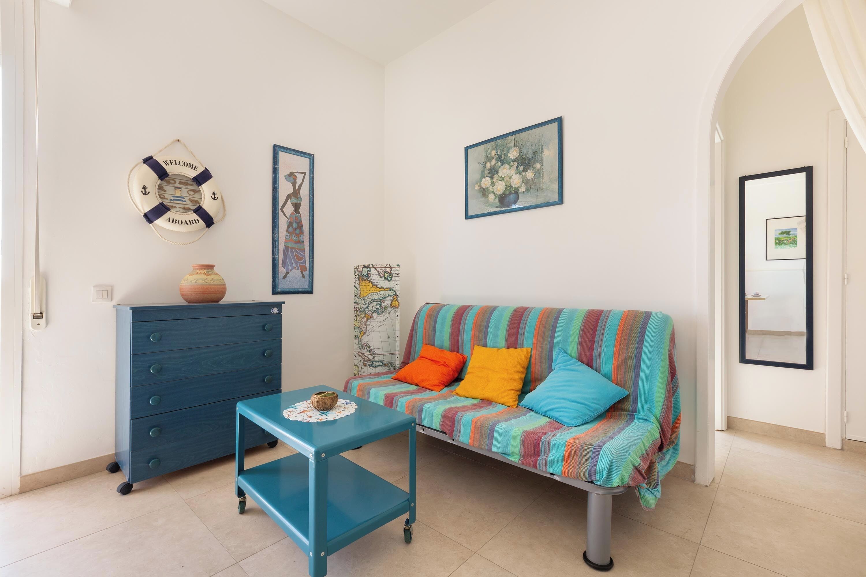 Ein Zimmer mit einem gestreiften Sofa, einem blauen Schrank, einem kleinen Tisch und einer Rettungsboje als Dekoration.