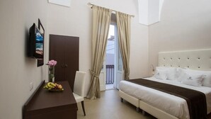 A hotel room with a bed, a desk with a TV, a chair, and a balcony with curtains. - Palazzo Perla - Junior Suite con Balcone (Gallipoli)