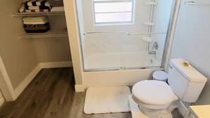 A compact bathroom with a shower, toilet, and storage shelves. - Charming 1 bed suite with AC and WiFi in Lakeland (Lakeland)