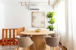 A dining area with a round wooden table, two chairs, a wooden bench, a potted plant, and a wall-mounted air conditioner.
