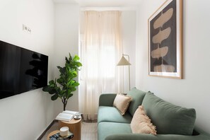 A living room with a flat-screen TV, a green sofa, a potted plant, a lamp, and a framed abstract artwork.