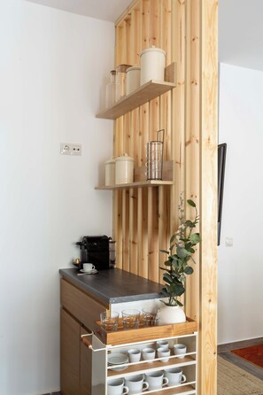A kitchen area with wooden shelves, a coffee machine, and a plant.