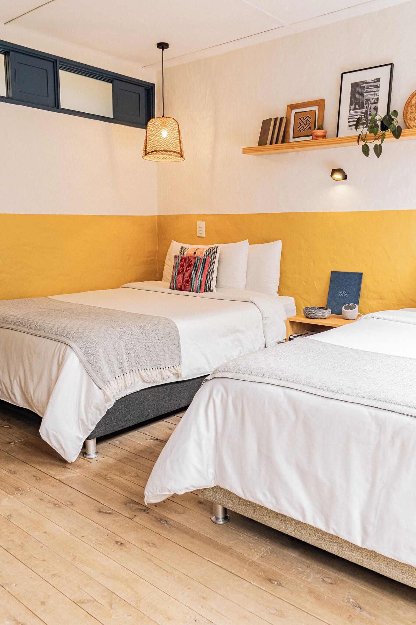 Una camera d'albergo con due letti, un pavimento in legno, una lampada a sospensione e uno scaffale con oggetti decorativi.