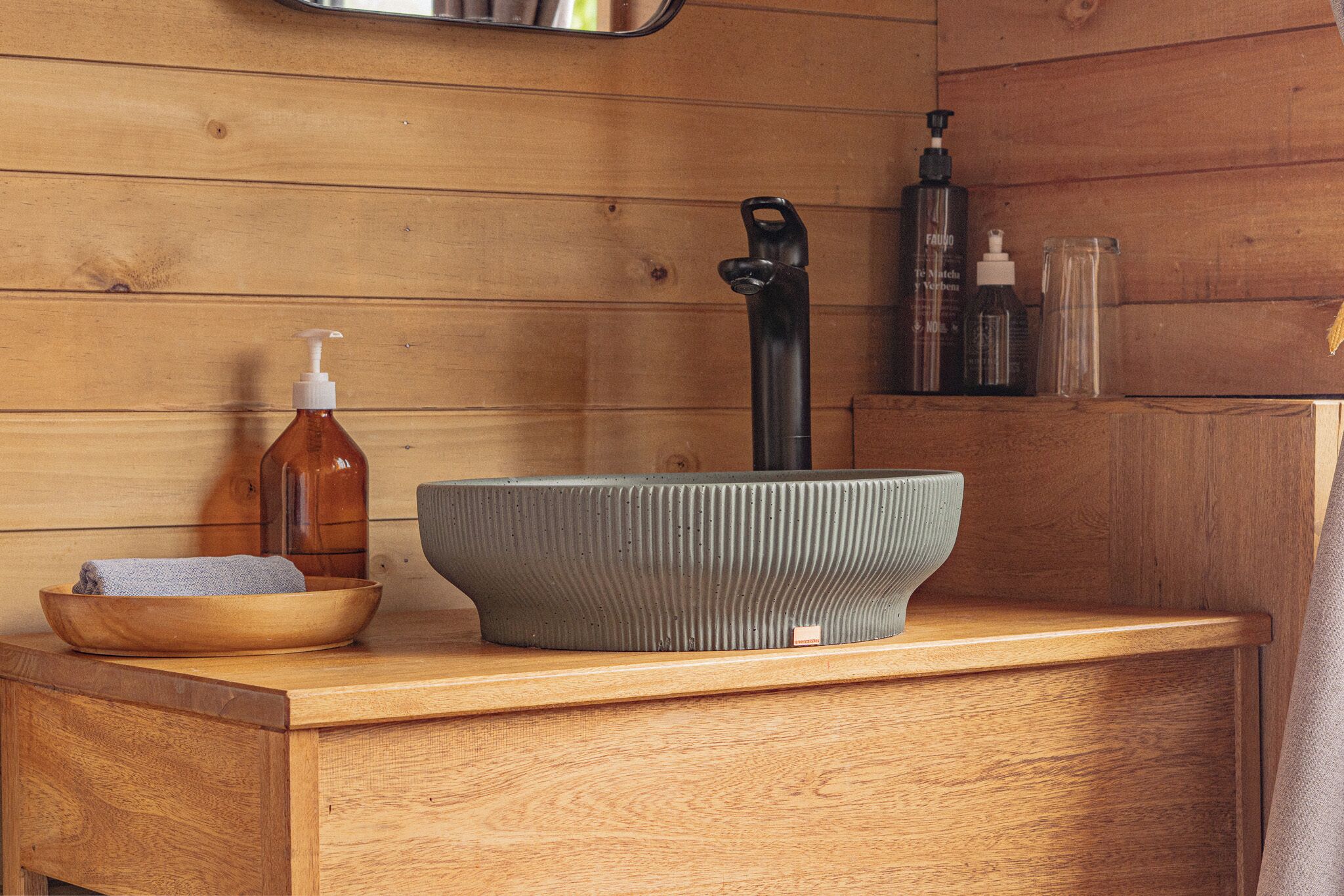 A wooden vanity with a large bowl, a pump bottle, and a black faucet.