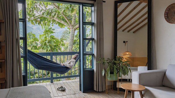 Una habitación con una hamaca, un sofá, una mesita y un ventanal con vistas a la vegetación.
