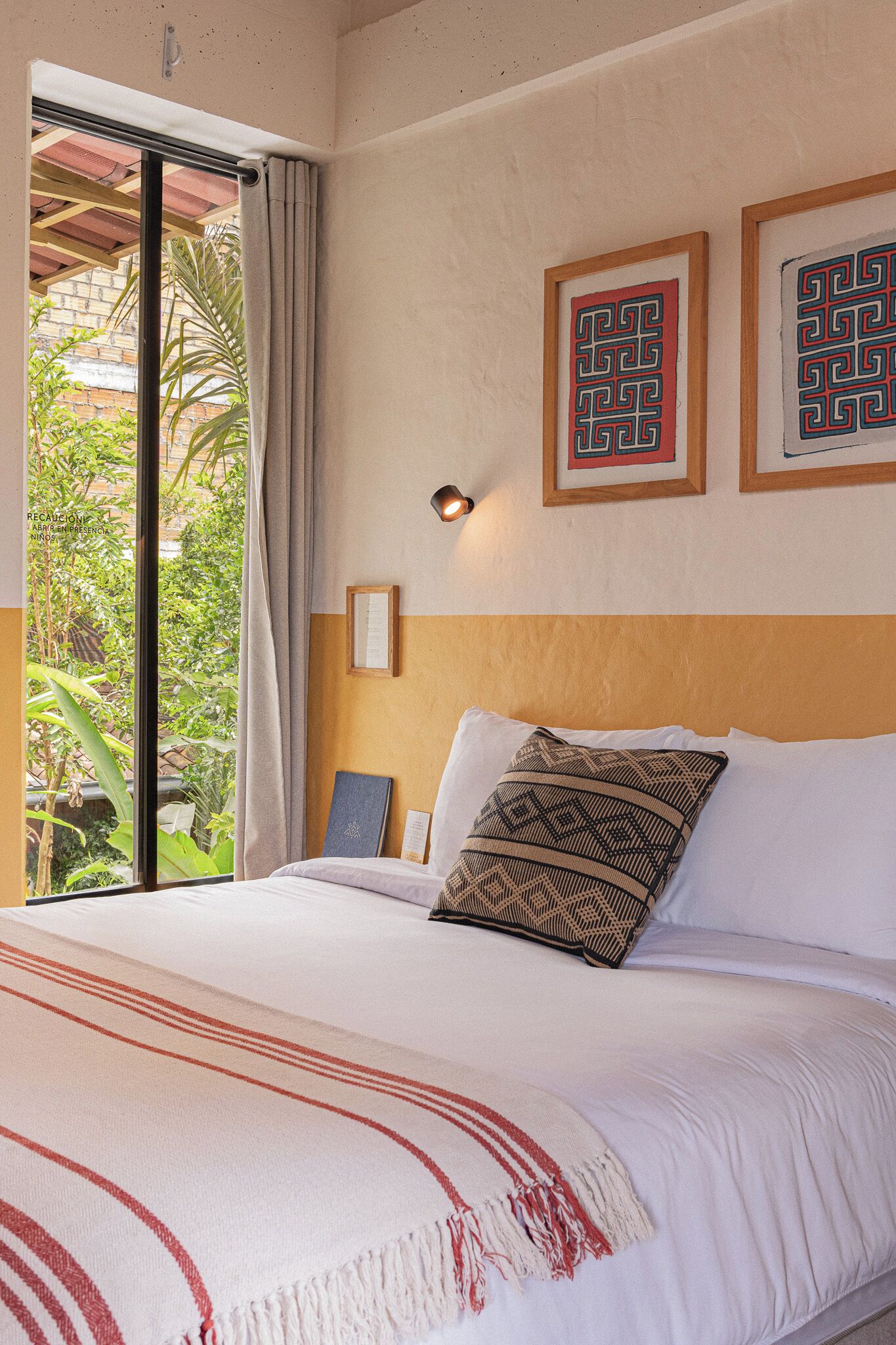 A bedroom with a bed, a window with curtains, and two framed wall art pieces.