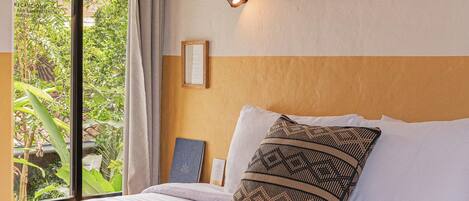 A bedroom with a bed, a window with curtains, and two framed wall art pieces.