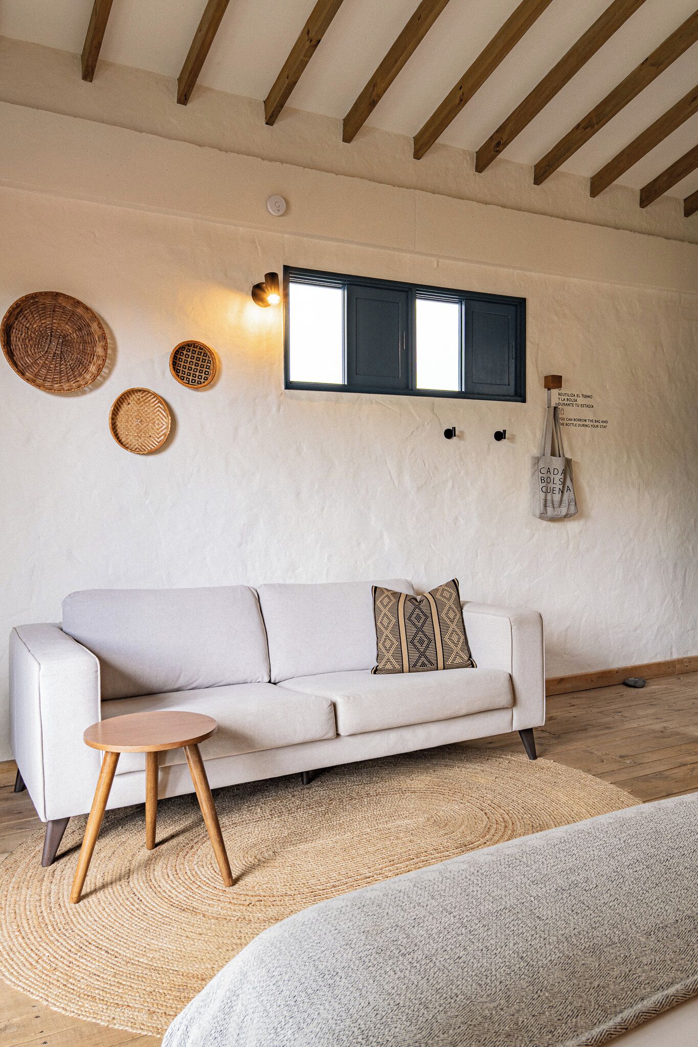 Una sala de estar moderna con un sofá, un taburete de madera, un tapete tejido y un televisor montado en la pared.
