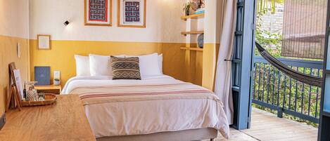 A bedroom with a bed, wooden bedside table, and a view of a balcony with a hammock.