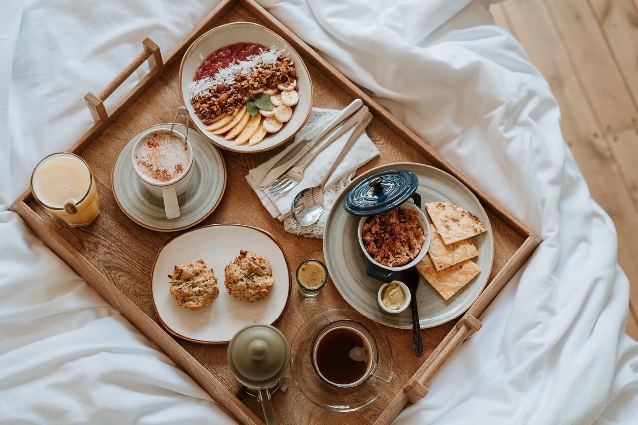 A wooden tray with breakfast items including pancakes, scones, and toast, accompanied by a cup of coffee and a glass of orange juice.