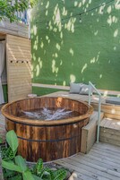 A wooden hot tub with a wooden deck, a green wall, and a string of lights.