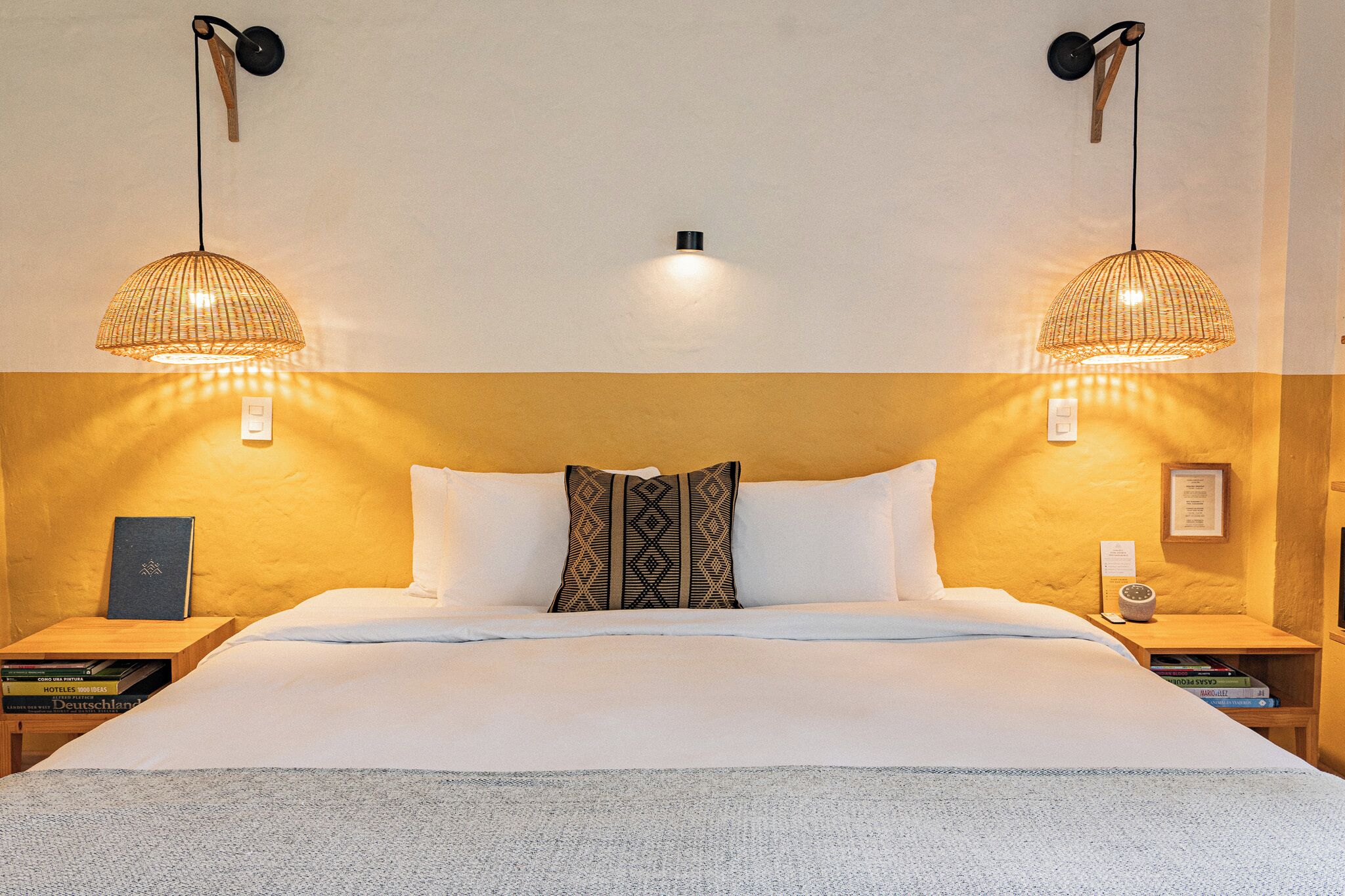 A hotel room with a large bed, two bedside tables, a nightstand, a wall-mounted lamp, and a wall clock.