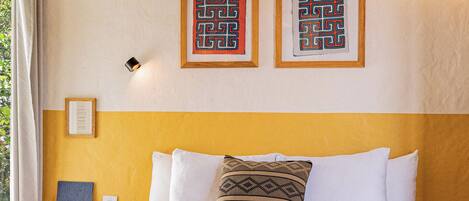 A bed with white bedding, a yellow headboard, and two framed wall art pieces.