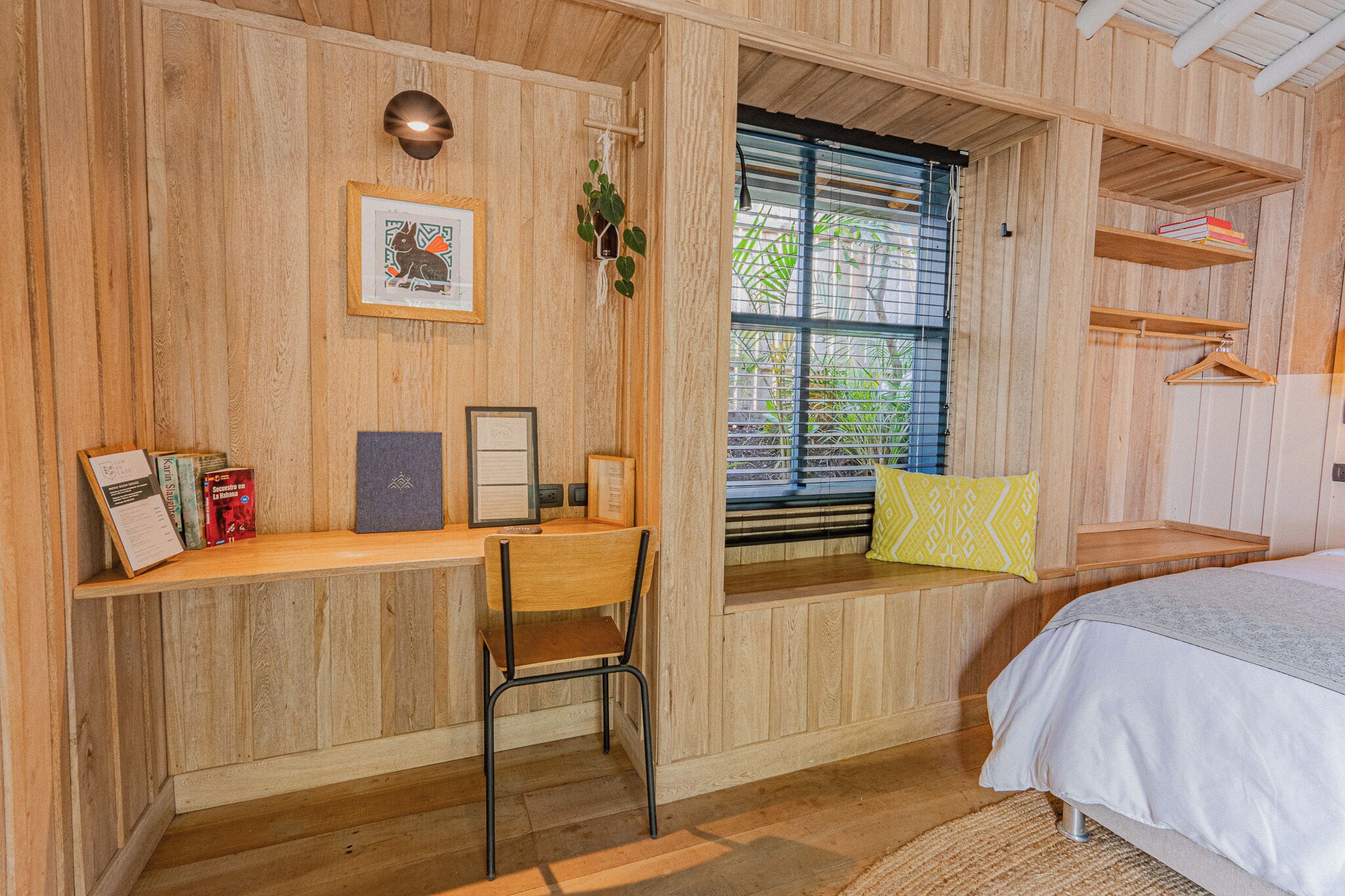A wooden room with a desk, chair, bed, window, and shelves.