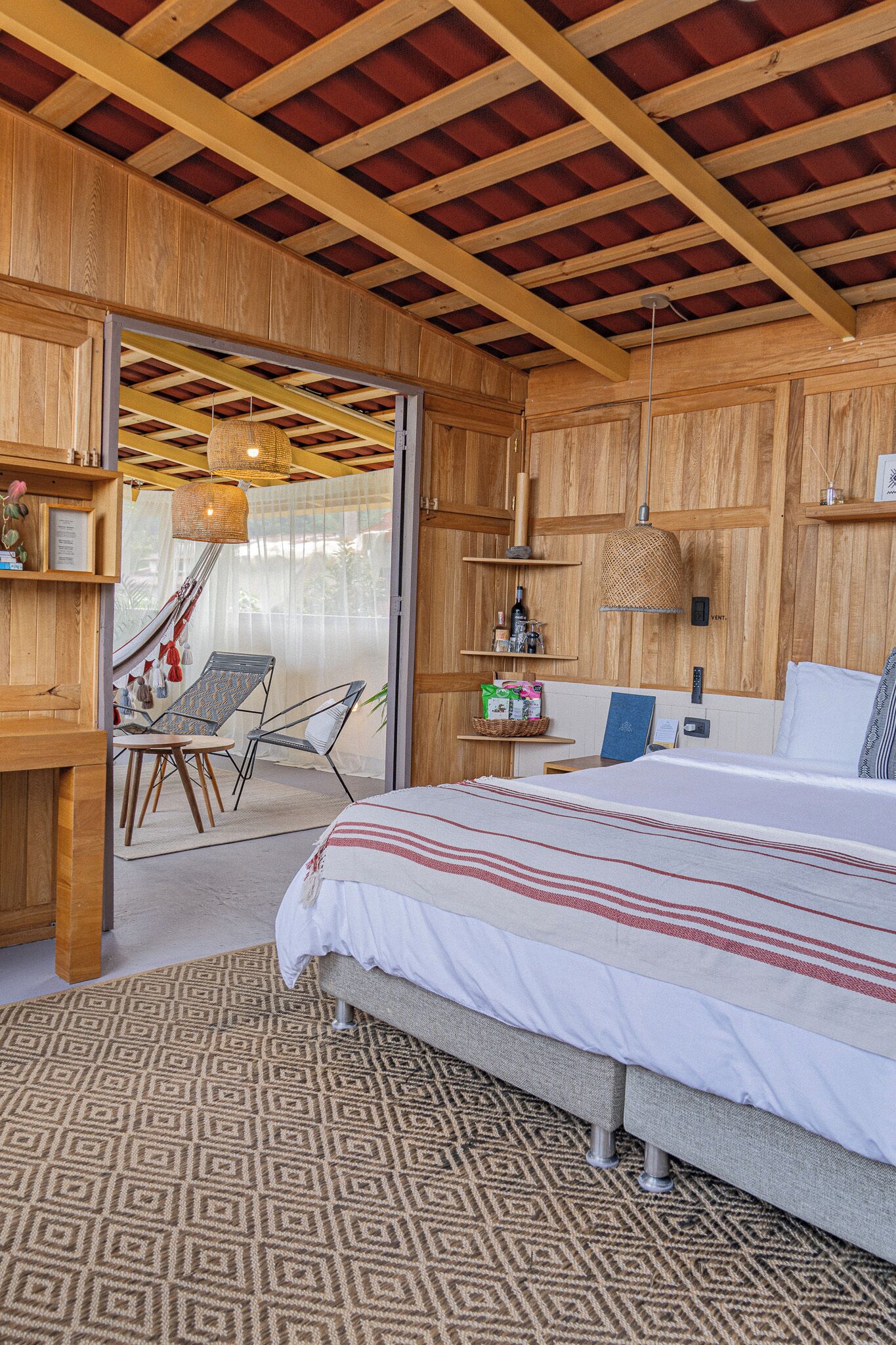 A wooden room with a bed, a hammock, a chair, and a table.