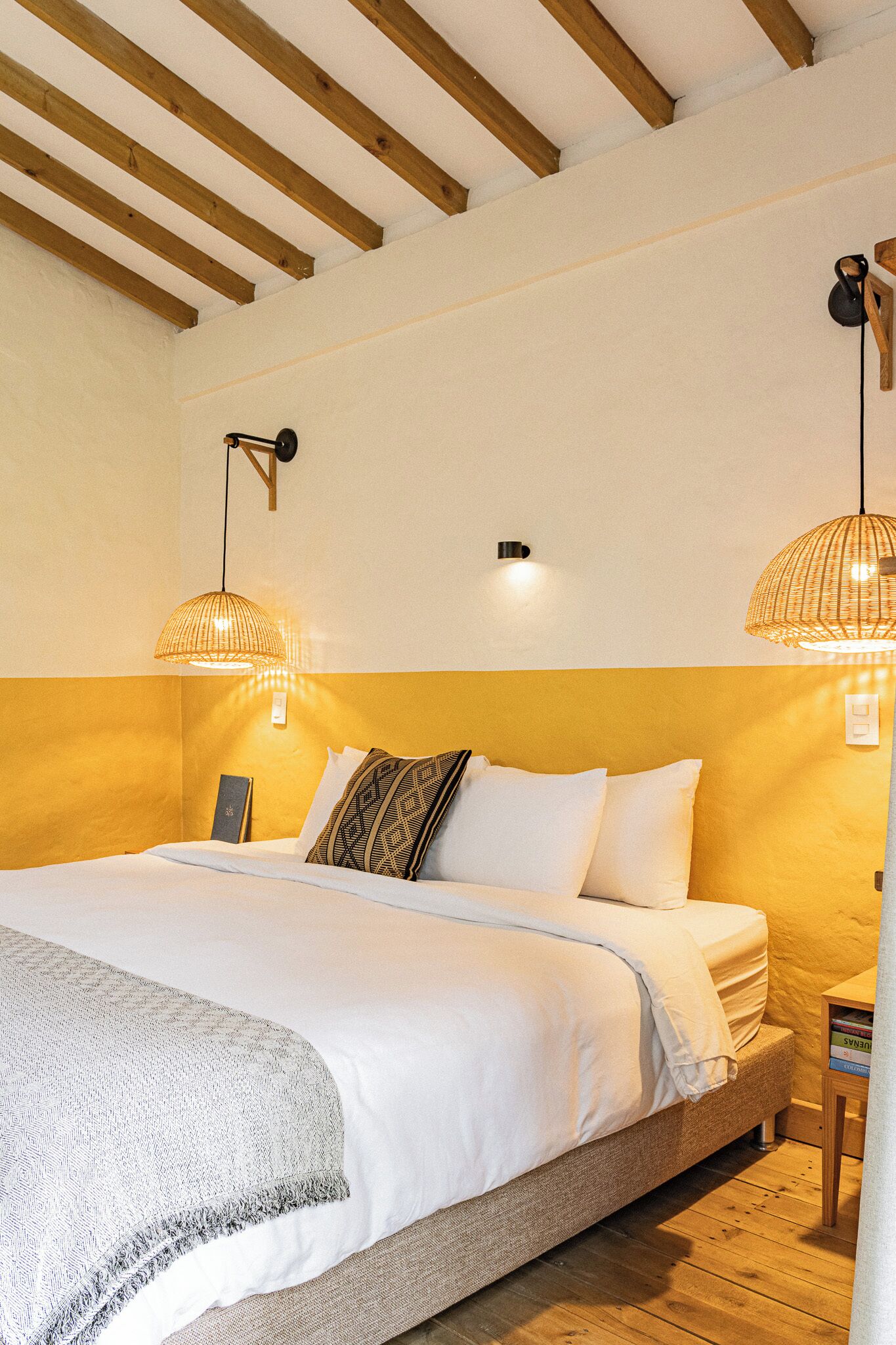 Una camera da letto con un letto, due lampade a parete, un soffitto in legno e un comodino con dei libri.