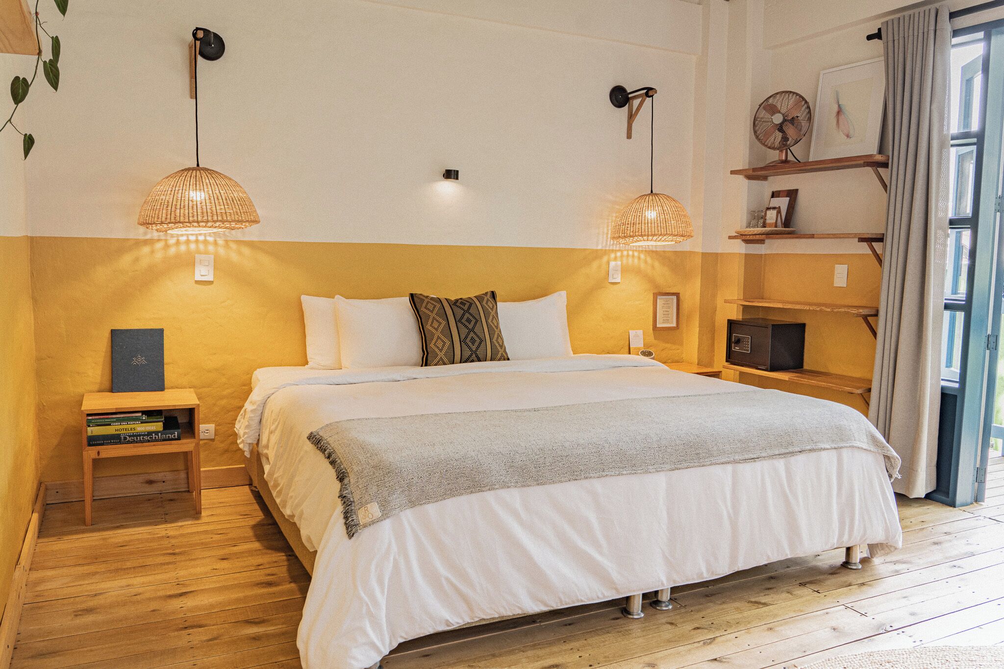 A bedroom with a bed, bedside tables, a wall-mounted fan, and a shelf with a fan and picture.