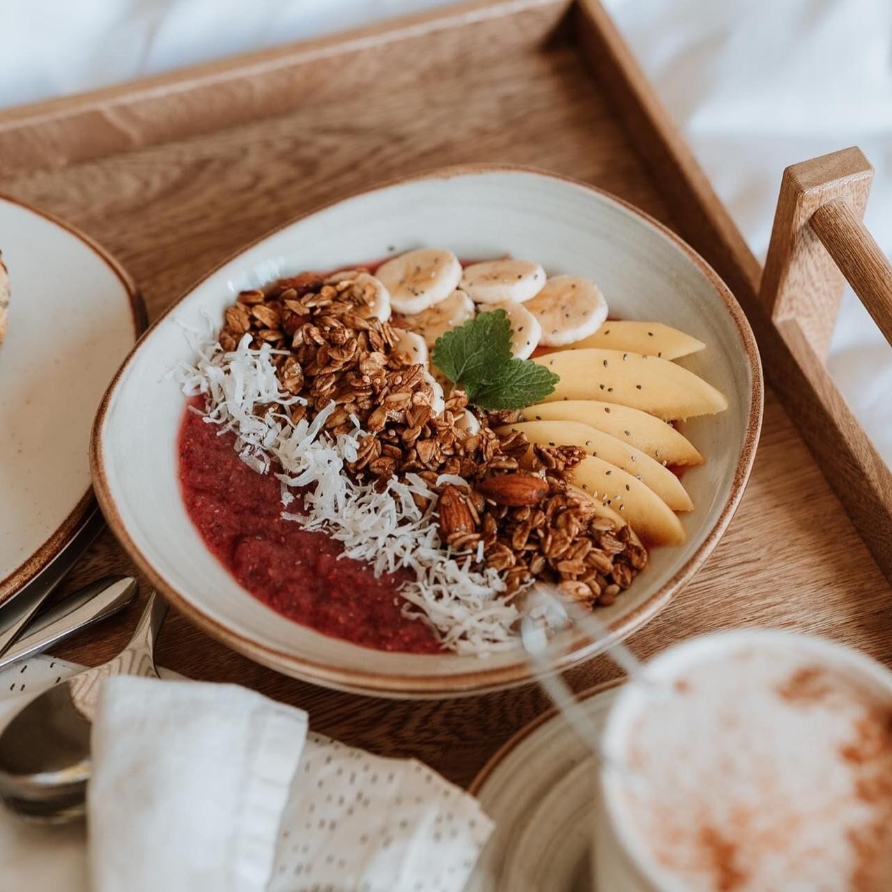 Bandeja de desayuno con granola, rodajas de plátano, coco rallado y salsa roja, acompañada de una taza de café.