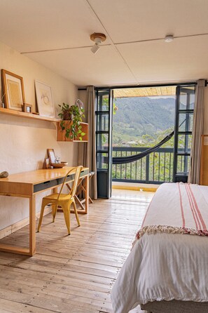 Ein Zimmer mit Schreibtisch aus Holz, einem Bett, einer Hängematte und Blick ins Freie.