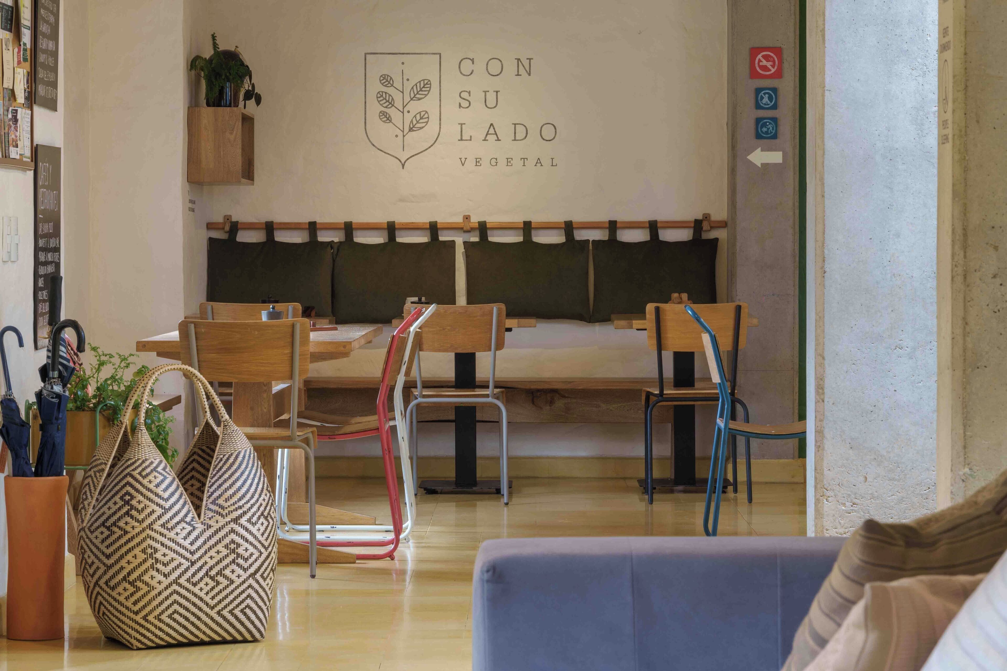 Interior de restaurante con zona de estar con bancos de madera, un tablero de menú colgado en la pared y una planta en la pared.
