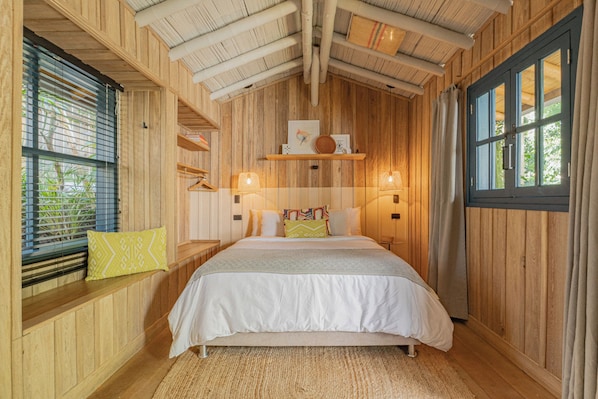 Ein Schlafzimmer mit Holzwänden, einem Bett, Nachttischlampen, einem Fenster mit Jalousien und einer Tür.