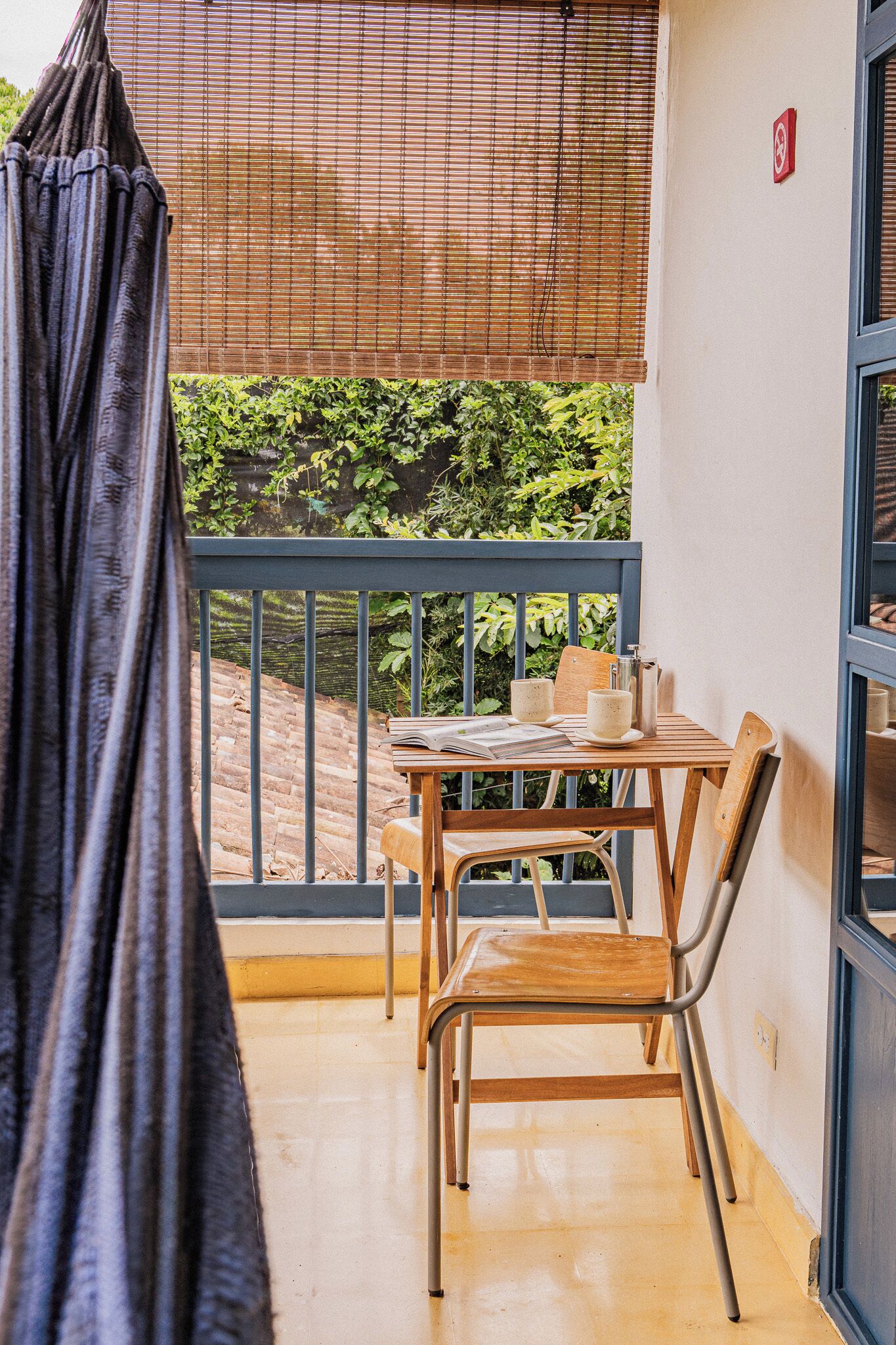 Un balcón con una mesa, sillas y una ventana que da a vistas de follaje.