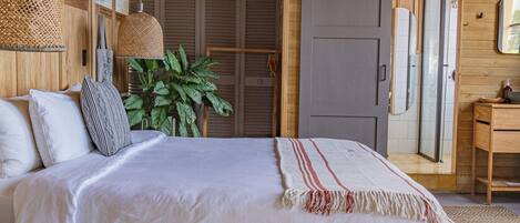 A bedroom with a large bed, wooden ceiling beams, a potted plant, a door, and a small table.