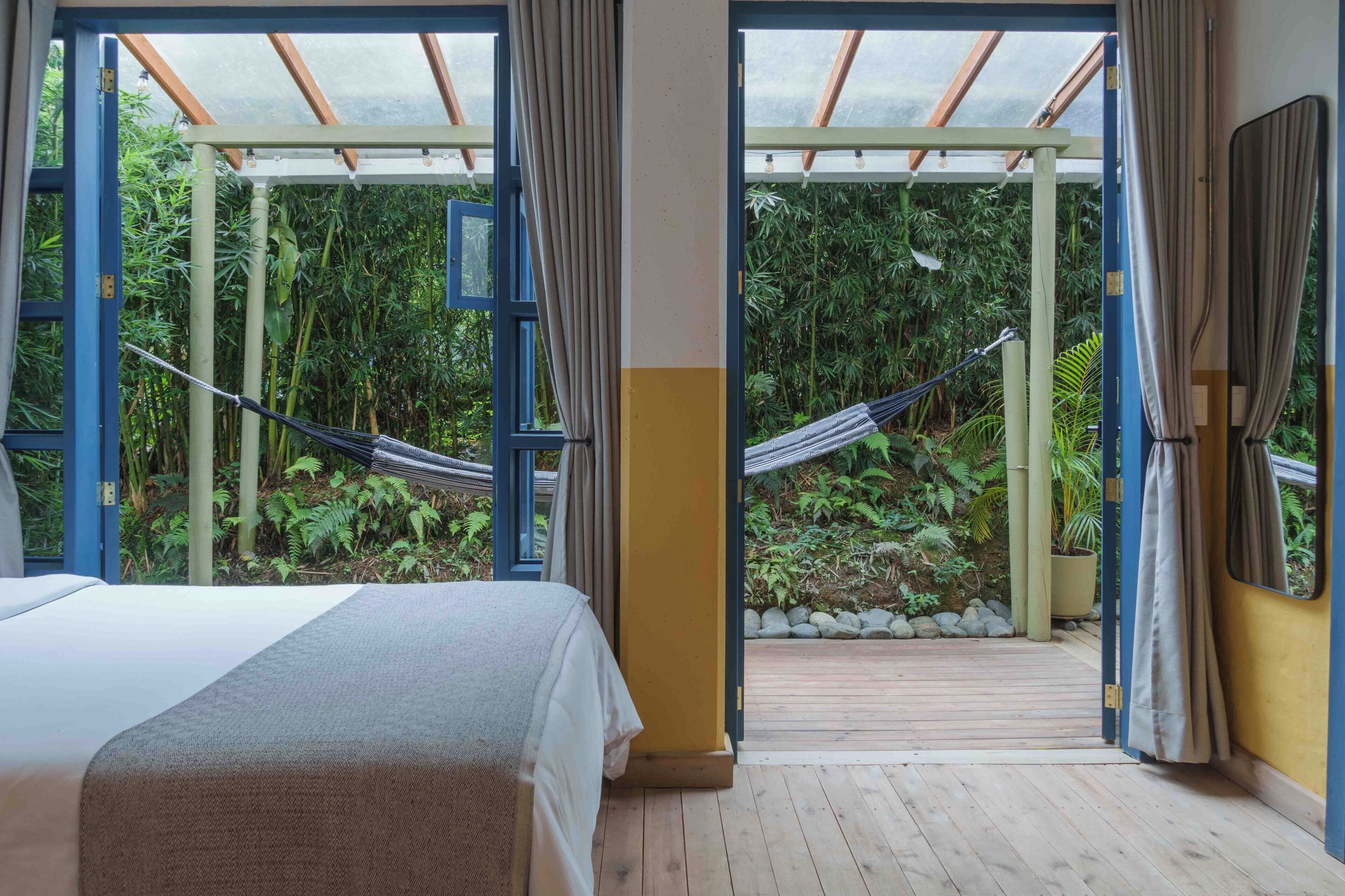 Een kamer met een bed, uitzicht op een tuin door een geopende deur, en een hangmat buiten.